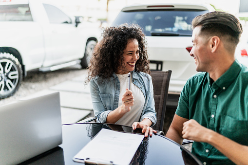 Mid adult couple signing documents to buy a car at dealership