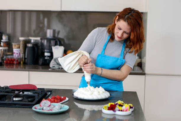 femme ajoutant de la crème fouettée à un gâteau - baking cake making women photos et images de collection