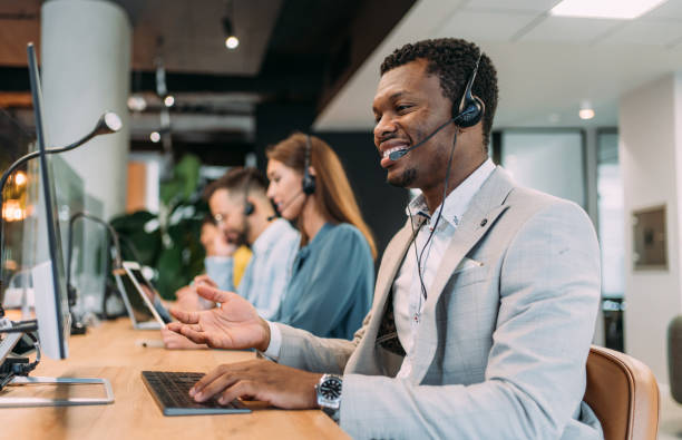 Call center workers. Shot of call center operators working in the office. Call center agent working with his colleagues in modern office. Smiling handsome businessman working in call center. sales executive stock pictures, royalty-free photos & images