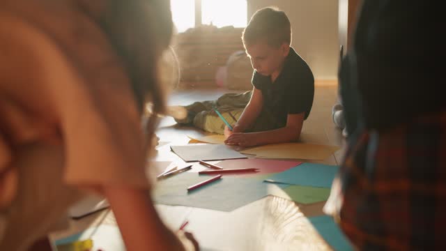 A group of preschool children draw on multi-colored sheets of paper using multi-colored pencils in a sunny room in a group at a children's school preparation club