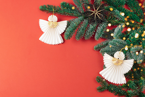 Christmas paper angels on the fir branch on red background. Christmas holiday concept. Top view, flat lay, copy space.