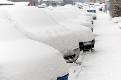 Snow covered cars parked in a row next to each other. Cars on the street in cold winter.
