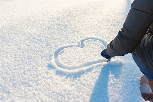 Woman drawing a heart on the snow.A woman wears blue gloves.Walentines day concept.