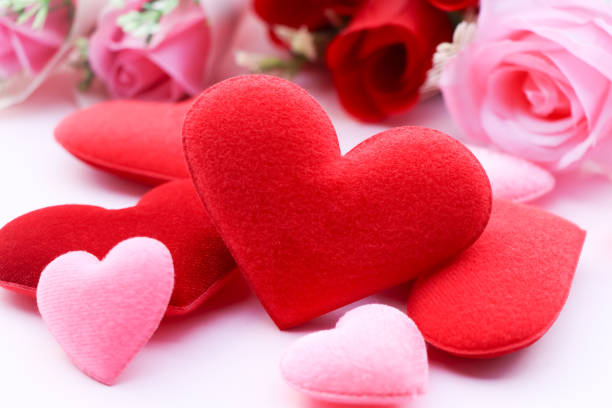 A heart shape cut out of pink paper that exposes a bed of red roses.