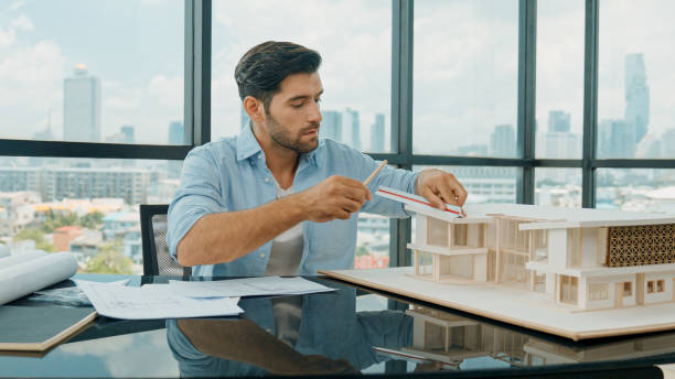 istock Skilled engineer looking at blueprint while measure house model. Tracery 1837551264