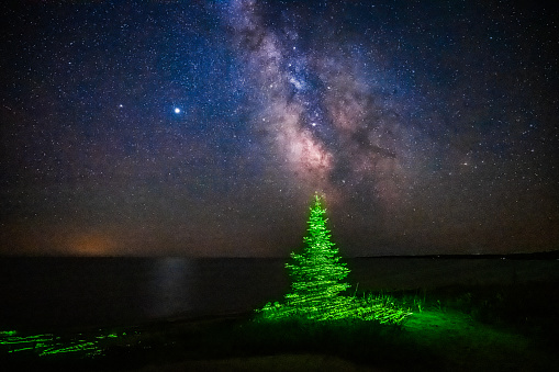 A eight second time exposure caught the milkyway over Lake Michigan. The pine tree stands near the beach and was light painted using a green laser.