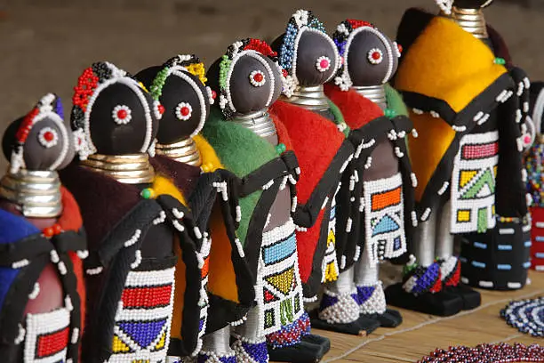 "A row of intricately beaded and clothed Ndebele dolls, dressed in the traditional tribal Ndebele clothing of the Ndebele tribe of South Africa. These dolls arehand made and for sale as souvenirs to tourists to the area. Photo has a shallow depth of field."