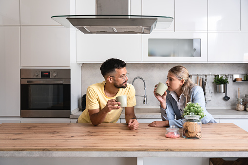Small talks. Man and woman standing in the kitchen chitchatting while they drinking coffee after female come back home from her workplace. Businesswoman and her roommate relaxing afternoon