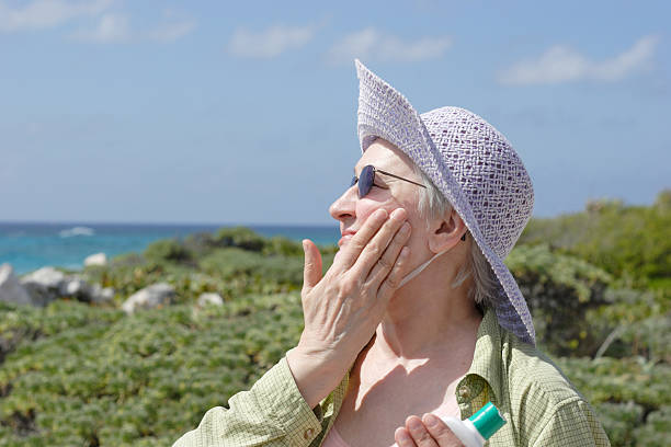 Sun Protection - Woman in Sunhat and Sunglasses Applying Sunscreen stock photo