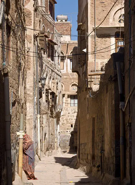"Beautiful street in old city in Sanaa.  in the evening, high angle view. Yemen. Image is framed by a shadow and  unrecognizable woman is  entering the house."