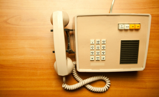 An old yellow and brown 1970's style phone sits on an office desk.  Horizontal with copy space.