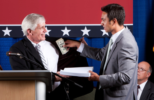 Lobbyist delivers prepared policy documents to man at podium as he simultaneously slips bribe money into the politician's inside coat pocket.