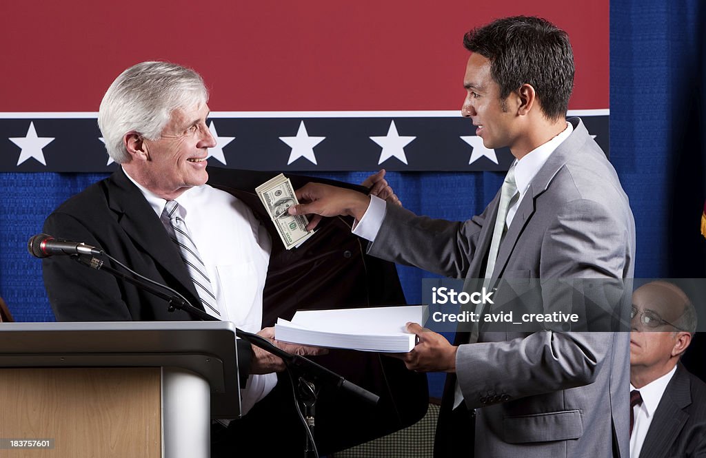 Politician Bribed by Lobbyist Lobbyist delivers prepared policy documents to man at podium as he simultaneously slips bribe money into the politician's inside coat pocket. Lobbying Stock Photo