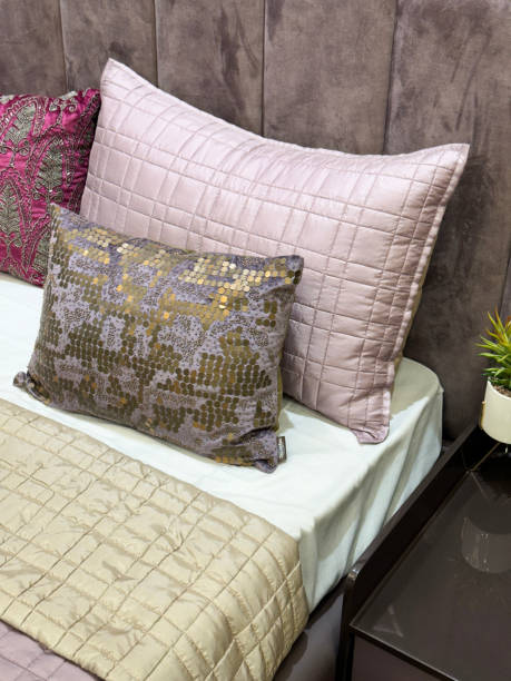 istock Image of double bed with padded, material covered headboard, quilted pillows, folded quilt cover, potted plant on nightstand with drawers, patterned scatter cushions, focus on foreground, elevated view 1837581185