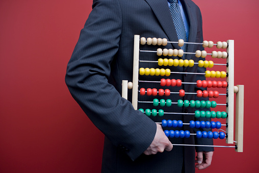 Humorous photo of a business man or accountant wearing a suit and tie holding an old fashioned vintage abacus for calculating numbers and doing accounting, finances, and taxes
