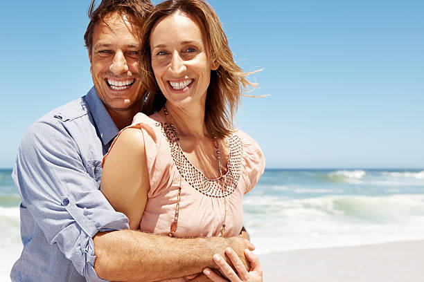 istock Man embraces woman in his arms as waves roll in behind them 183758994