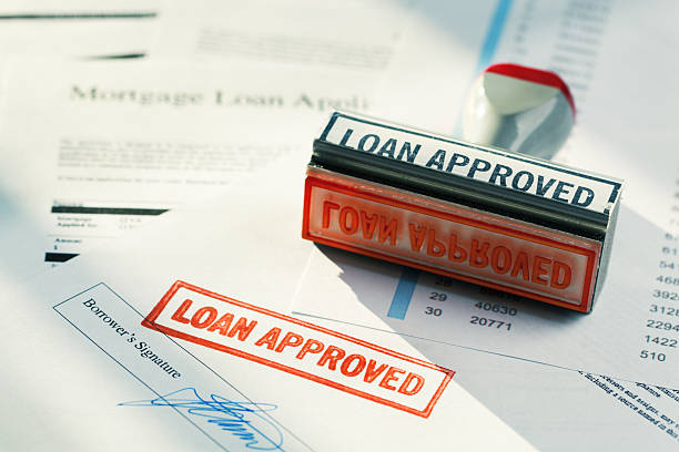 “LOAN APPROVED” Approval Red Rubber Stamp Approving Mortgage Application Document "Subject: Horizontal view of a rubber stamper with the words aLOAN APPROVEDaA resting on a pile of loan papers, including a borroweraas signature page stamped in red, showing approval was granted. Bright lighting and long shadows create a positive mood." mortgage document photos stock pictures, royalty-free photos & images