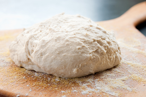 A blob of unbaked homemade boule dough sits on a wood paddle.