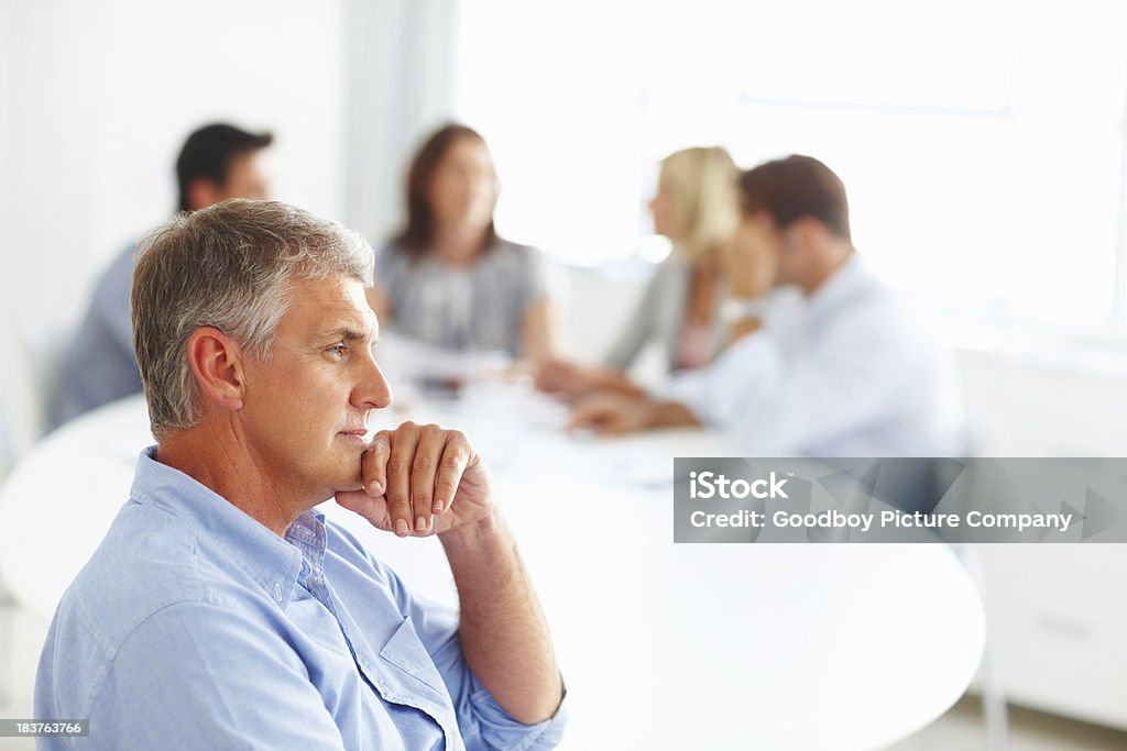 Thoughtful businessman Portrait of mature thoughtful businessman with colleagues in background 50-59 Years Stock Photo