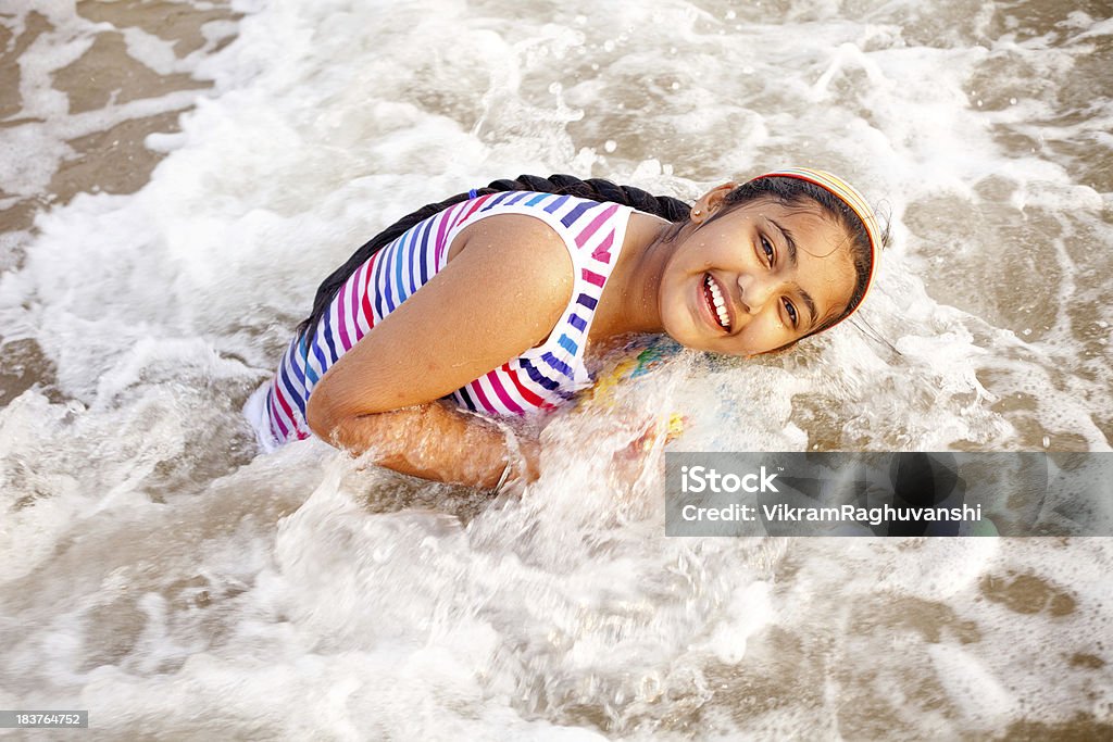 Un alegre Little india niña jugando en la playa disfrutando de las olas - Foto de stock de Vadear libre de derechos