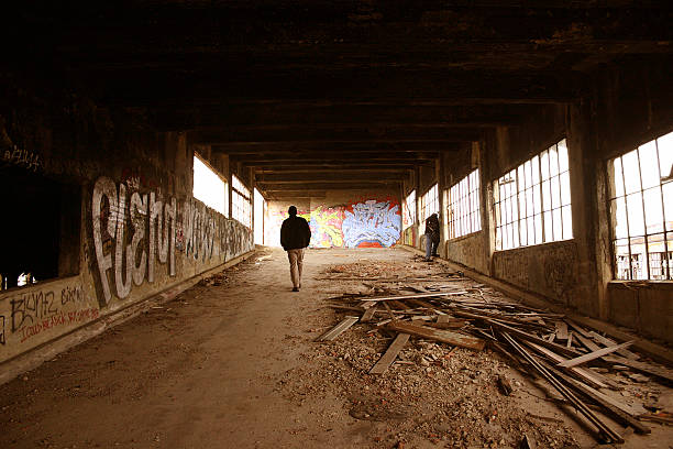 Detroit Packard Plant "Passerby wander up a ramp at the abandoned Detroit Packard Plant in Detroit, Michigan.Image has a gritty, grungy, textured feel.Acceptable street-graffiti is shown.People pictured are unidentifiable." detroit ruins stock pictures, royalty-free photos & images