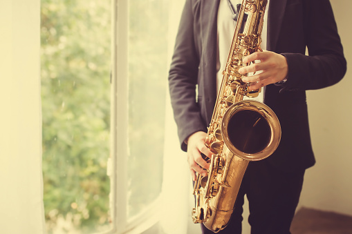 close up of Young Saxophone Player hands  playing tenor sax musical instrument over concrete wall with window light,  closeup with copy space, vintage tone,  can be used for music background