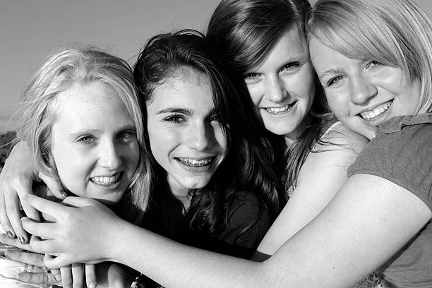 A close up portrait of four beautiful teen girls hugging each other and smiling at the camera.