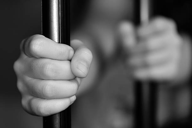 Hands of a child behind bars in grayscale stock photo