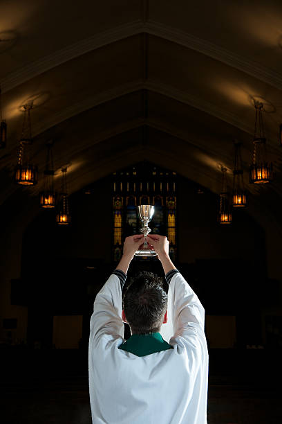 Blessing of Wine for Communion in Darkly Lit Church Ancient Church with Priest Raising Silver Chalice toward heaven. anglican eucharist stock pictures, royalty-free photos & images