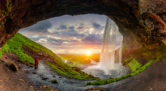 Majestic natural cave with sunset over Seljalandsfoss waterfall flowing and tourist enjoying in summer at South of Iceland
