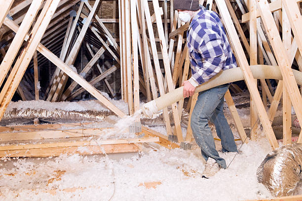 Trabajador de pulverización aislamiento de fibra de vidrio soplado entre ático Trusses - foto de stock