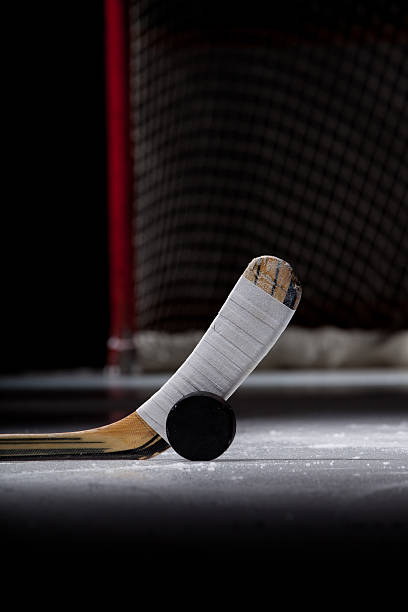 Ice Hockey Puck and Stick An ice hockey puck and stick are dramatically lit in the foreground while an open hockey net is in the background.  Captured with a Canon 5D Mark II. hockey puck photos stock pictures, royalty-free photos & images