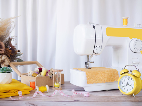 Sewing machine working with yellow fabric, sewing accessories on the table, stitch new clothing.