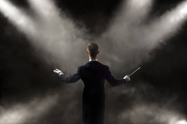Orchestra Conductor Male conductor stands on foggy background with stage lighting.Visible fog and noise. musical conductor stock pictures, royalty-free photos & images