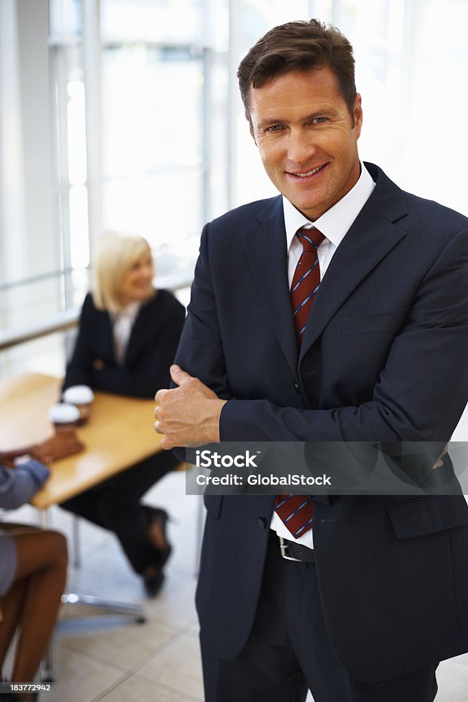 Business man taking break from work Handsome business man with hands folded with colleagues in background 40-49 Years Stock Photo