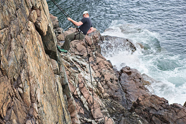 escalar rochas em um penhasco acima do oceano no maine - climbing men sea cliff imagens e fotografias de stock