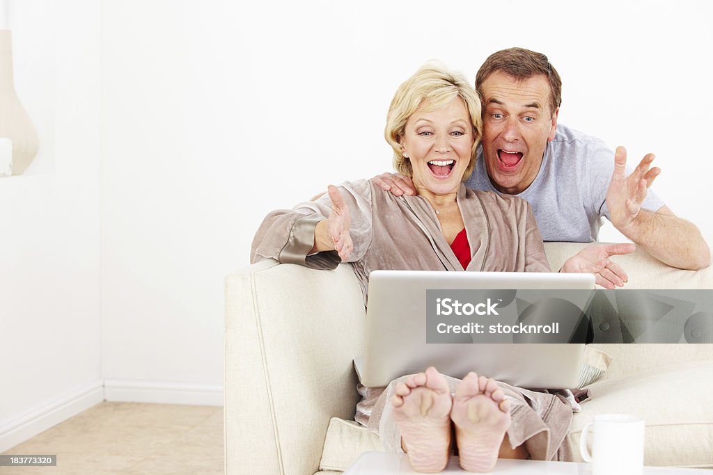 Pareja madura feliz usando una computadora portátil en la sala de estar - Foto de stock de 50-59 años libre de derechos