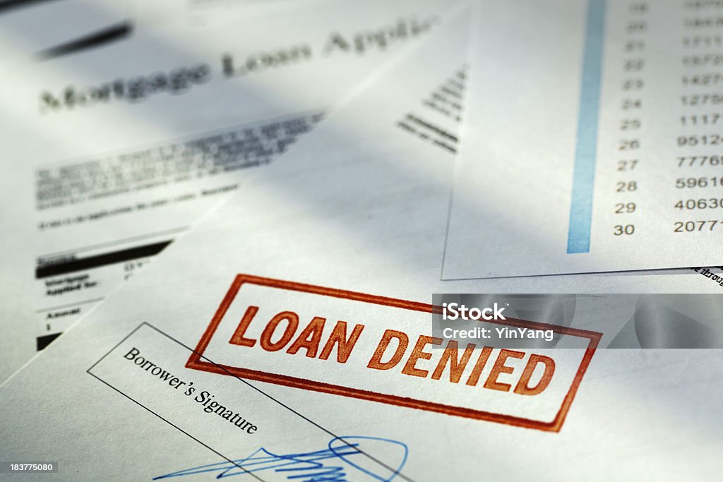 Mortgage Application Borrower Document with “Loan Denied” Red Rubber Stamp Subject: Horizontal view of the words aLOAN DENIEDaA stamped in red ink on the borroweraas signature page in a pile of mortgage loan application papers. Rejection Stock Photo