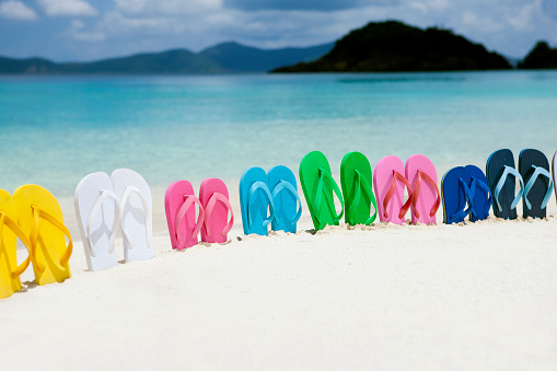 Flip-flops on beach sand beside word Summer