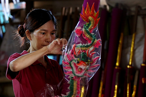 An Asian woman is using plastic to wrap finished product of Dragon Sculpture Joss stick in factory