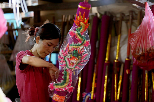 An Asian woman is using plastic to wrap finished product of Dragon Sculpture Joss stick in factory