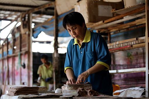 An Asian woman is moulding a shape of dragon in Joss stick factory daily production