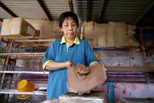 An Asian woman is moulding a shape of dragon in Joss stick factory daily production
