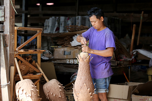 A Myanmar ethnicity man is working sculpting oversize pineapple shaped Joss stick factory daily production