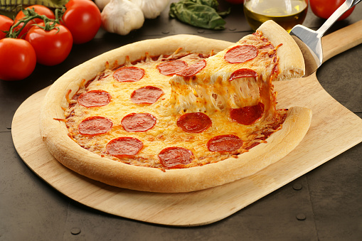 Slice of pepperoni pizza being lifted from a freshly baked whole pie.