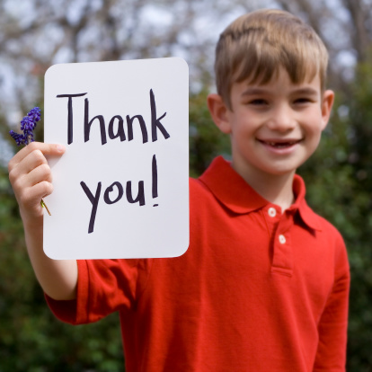 Cute young elementary age boy holding a sign that says thank you with flowers while smiling.
