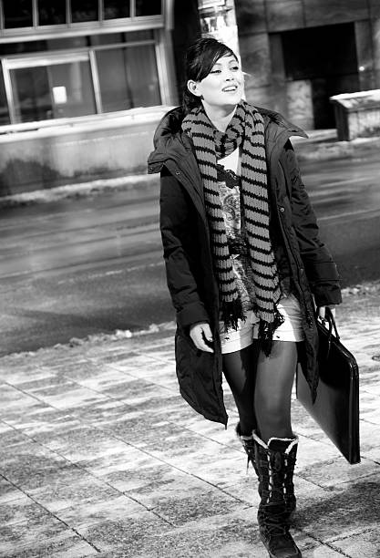 Black and white shot of beautiful young woman her purse while walking along city quay during sunny autumn day