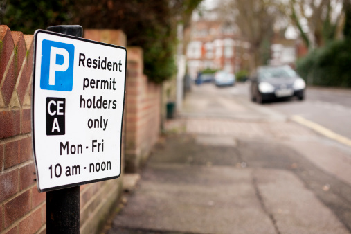 London suburban street scene with focus on an informational sign with details of parking restrictions.  The letters refer to the parking zones.