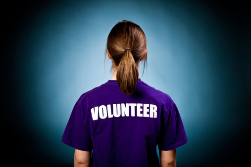A young woman wears a volunteer shirt against a blue spotlighted backdrop.