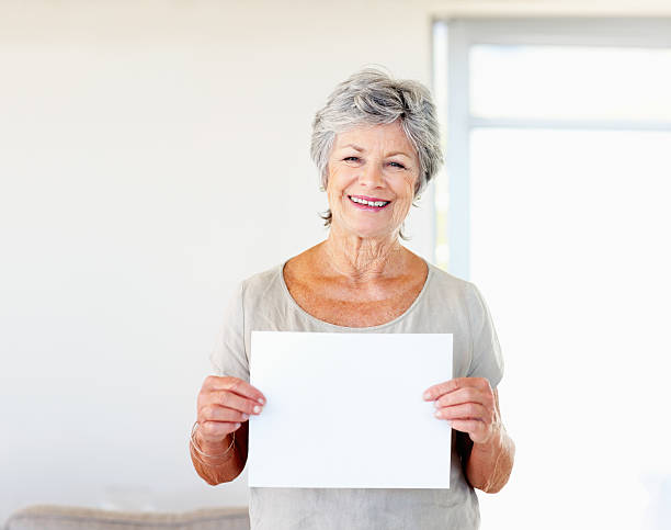 Woman holding blank sheet of paper Pretty elderly woman holding blank sheet of paper and smiling placard photos stock pictures, royalty-free photos & images